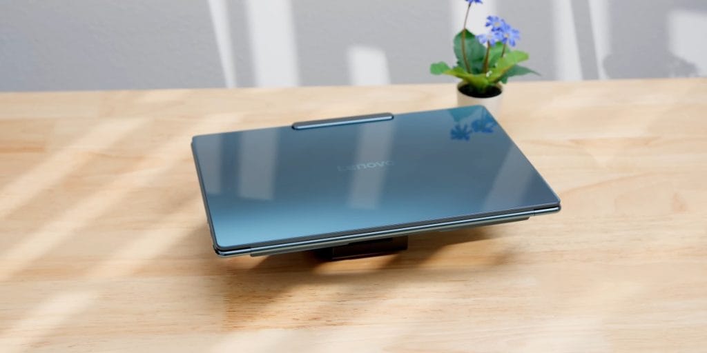 A closed, dark blue Lenovo Yoga Slim 9i laptop, propped up on a stand on a wooden table.